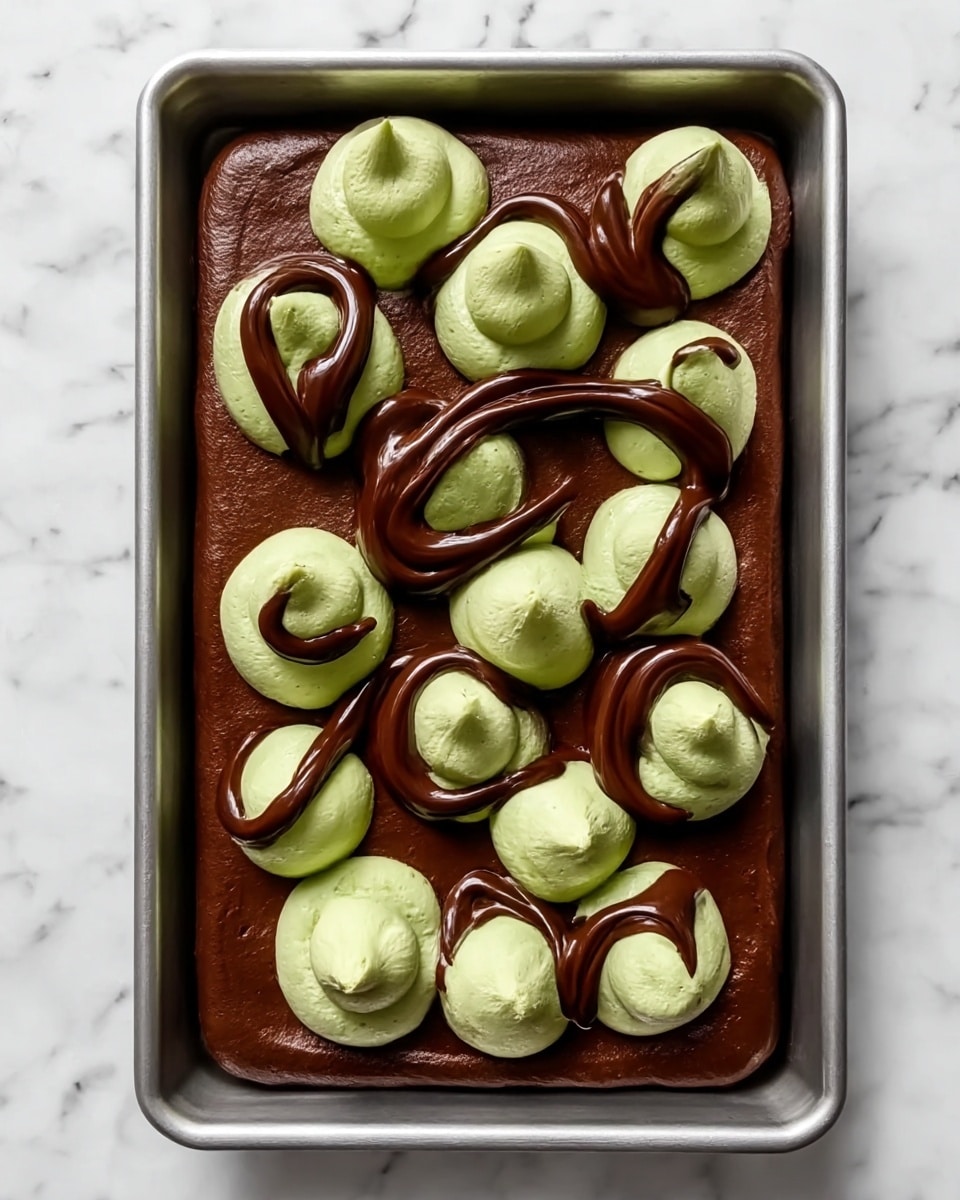 A rectangular metal tray filled with a smooth, thick dark brown chocolate layer as the base, covering the entire surface evenly. On top of this base, there are eleven dollops of light green cream spaced out in a slightly uneven grid, each dollop having a soft and fluffy texture with a small peak in the center. Over the green cream dollops, thick streams of glossy dark brown chocolate sauce are drizzled in looping, curved lines creating an artistic swirl pattern. The tray is placed on a white marbled surface. Photo taken with an iphone --ar 4:5 --v 7