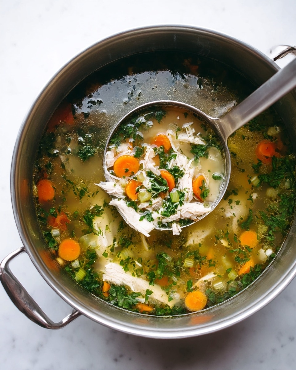 A large stainless steel pot filled with clear chicken soup containing shredded white chicken meat, slices of orange carrots, chopped green celery, and fresh green herbs floating on the surface; a long stainless steel ladle is in the pot lifting a mix of chicken, carrot, and greens; the pot sits on a white marbled surface photo taken with an iphone --ar 4:5 --v 7