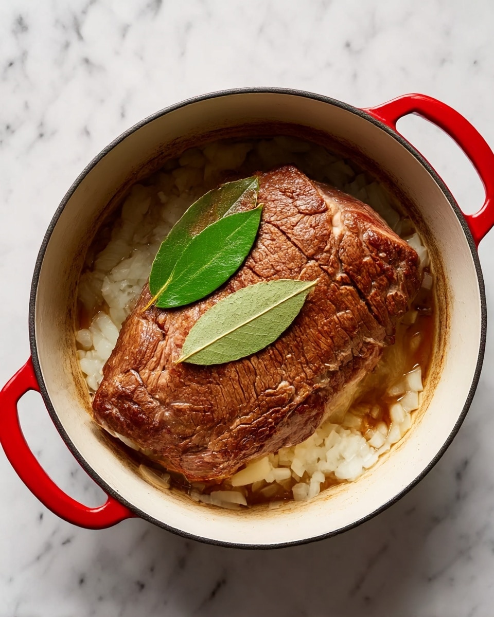 A large, browned piece of meat sits in the center of a white round pot with red handles on a white marbled surface. Beneath the meat is a layer of chopped white onions, slightly cooked and spread evenly along the bottom of the pot. On top of the meat lies a single fresh green bay leaf. The meat has a rough texture, with visible cooking marks and cracks. The lighting highlights the warm brown tones of the meat and the contrasting white onions below. Photo taken with an iphone --ar 4:5 --v 7