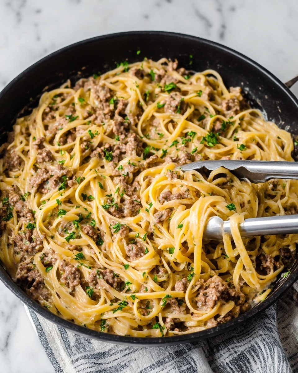 A black skillet filled with creamy pasta mixed with small chunks of browned ground meat, topped with fresh green parsley scattered evenly across the dish. The pasta strands are yellowish and coated in a light sauce, showing a soft and smooth texture. Silver metal tongs grip a portion of the pasta on the right side, with pasta strands draped over them. The skillet sits on a folded cloth with a striped pattern, all set on a white marbled surface. Photo taken with an iphone --ar 4:5 --v 7