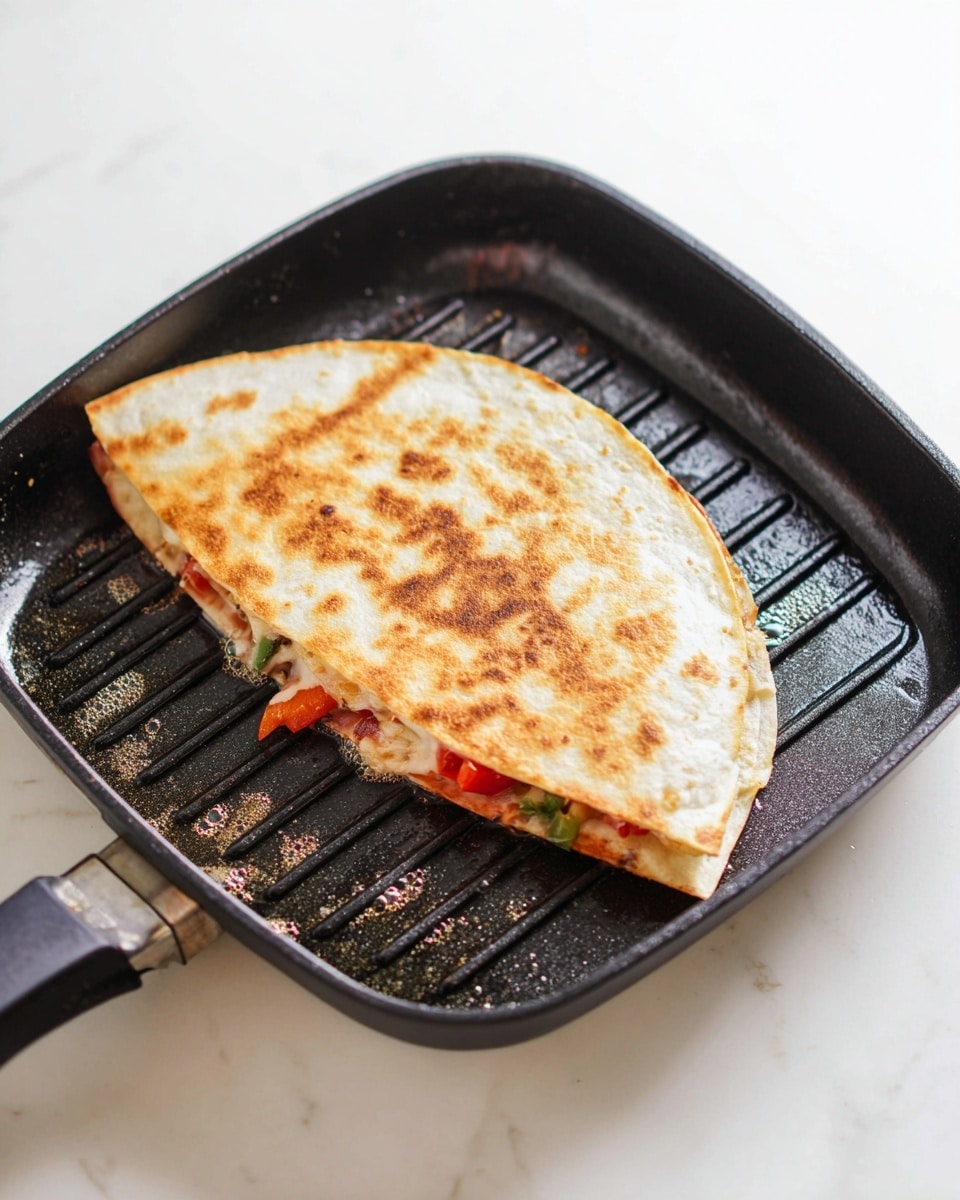 A golden brown folded quesadilla is cooking in a square black grill pan with ridges, showing slight browning and crispy spots on the top tortilla layer. Inside, you can see thin slices of green and red peppers and some melted cheese peeking out from the edges, giving a layered view of colorful filling beneath the warm, toasted tortilla. The pan sits on a white marbled surface, and slight bubbling butter or oil can be seen around the quesadilla in the pan. Photo taken with an iphone --ar 4:5 --v 7