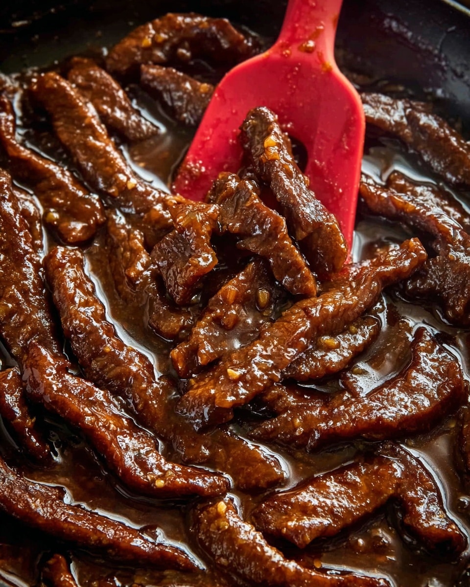 A close-up view of many dark brown beef strips in a thick, shiny, brown sauce covering them evenly. The beef strips are long and slightly curved with a moist, textured surface. A bright red silicone spatula is partially submerged among the beef, lifting some strips up. The background shows the beef and sauce filling a pan with a glossy surface. The photo is taken with an iphone --ar 4:5 --v 7
