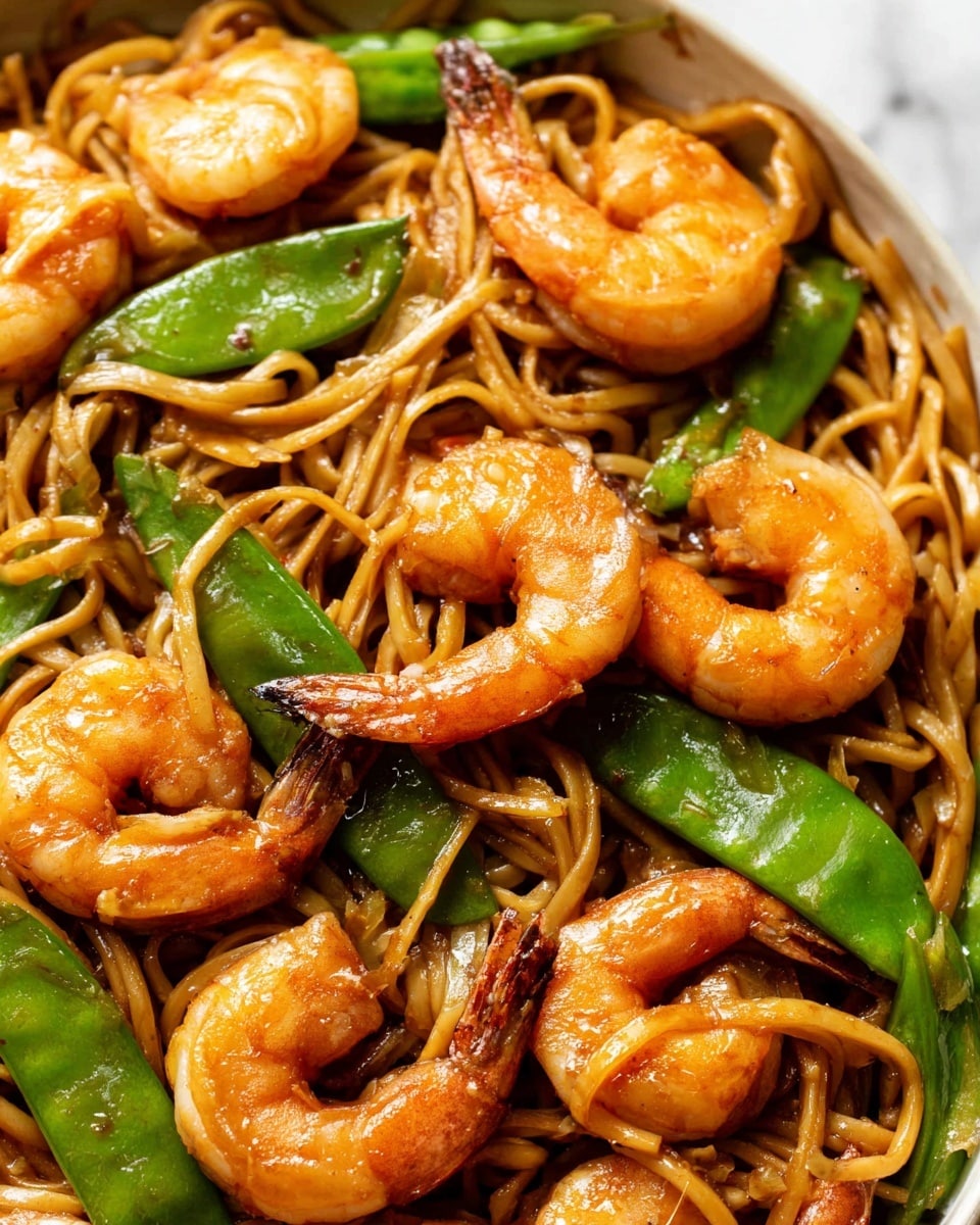 This close-up image shows a dish with three main layers: the bottom layer has long, light brown noodles that are slightly glossy and twisted together, the middle layer features bright green snap peas scattered throughout, and the top layer consists of medium-sized, orange shrimp with a shiny, cooked texture and slightly curled tails. The shrimp and snap peas rest evenly on the noodles, creating a colorful contrast between the light brown, green, and orange elements. The background is a white marbled texture, giving a clean, fresh look to the overall image. photo taken with an iphone --ar 4:5 --v 7