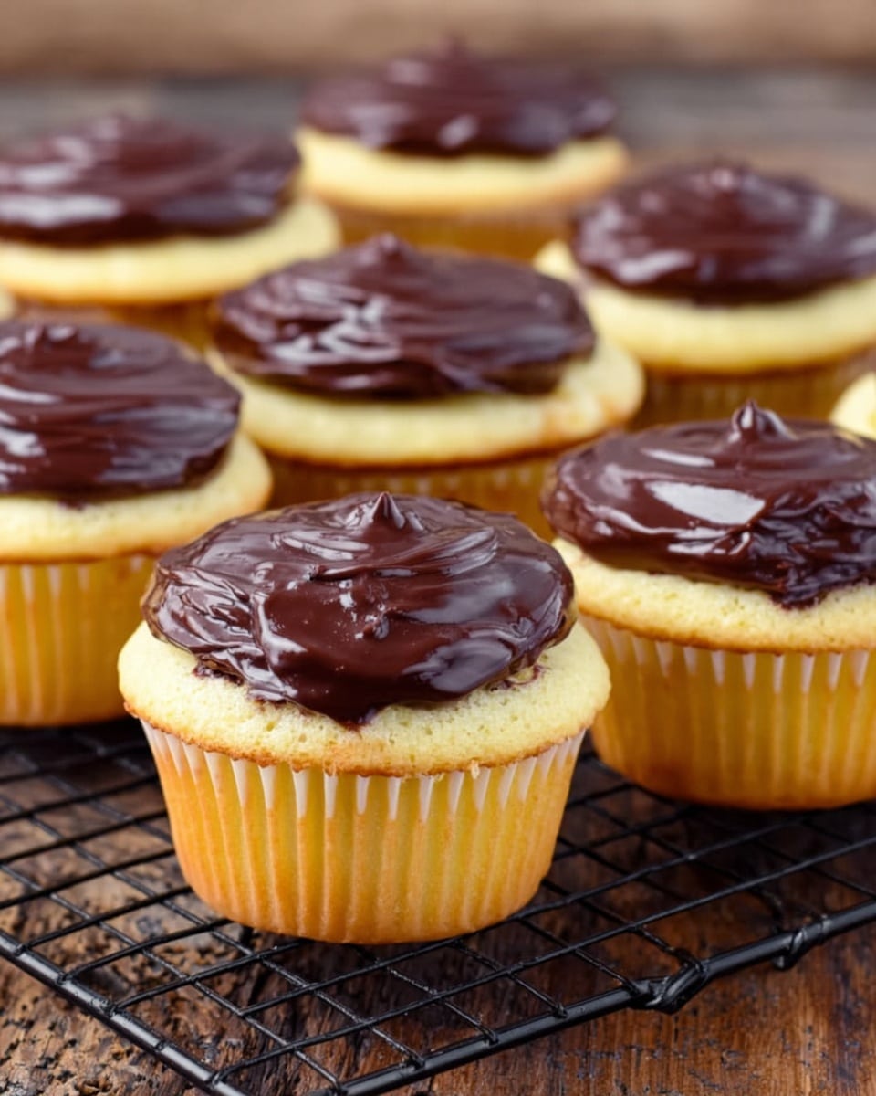 The image shows several vanilla cupcakes with a thick layer of dark chocolate frosting on top, placed evenly on a black cooling rack. The cupcakes have a light yellow base with soft swirl textures and are wrapped in light-colored paper liners. The dark chocolate frosting on top is shiny and smooth with some swirled peaks, giving it a rich look. The background is a rustic wooden table, but imagine it as a white marbled texture. All cupcakes are arranged closely in rows, filling the frame with a warm and tasty feel. Photo taken with an iphone --ar 4:5 --v 7