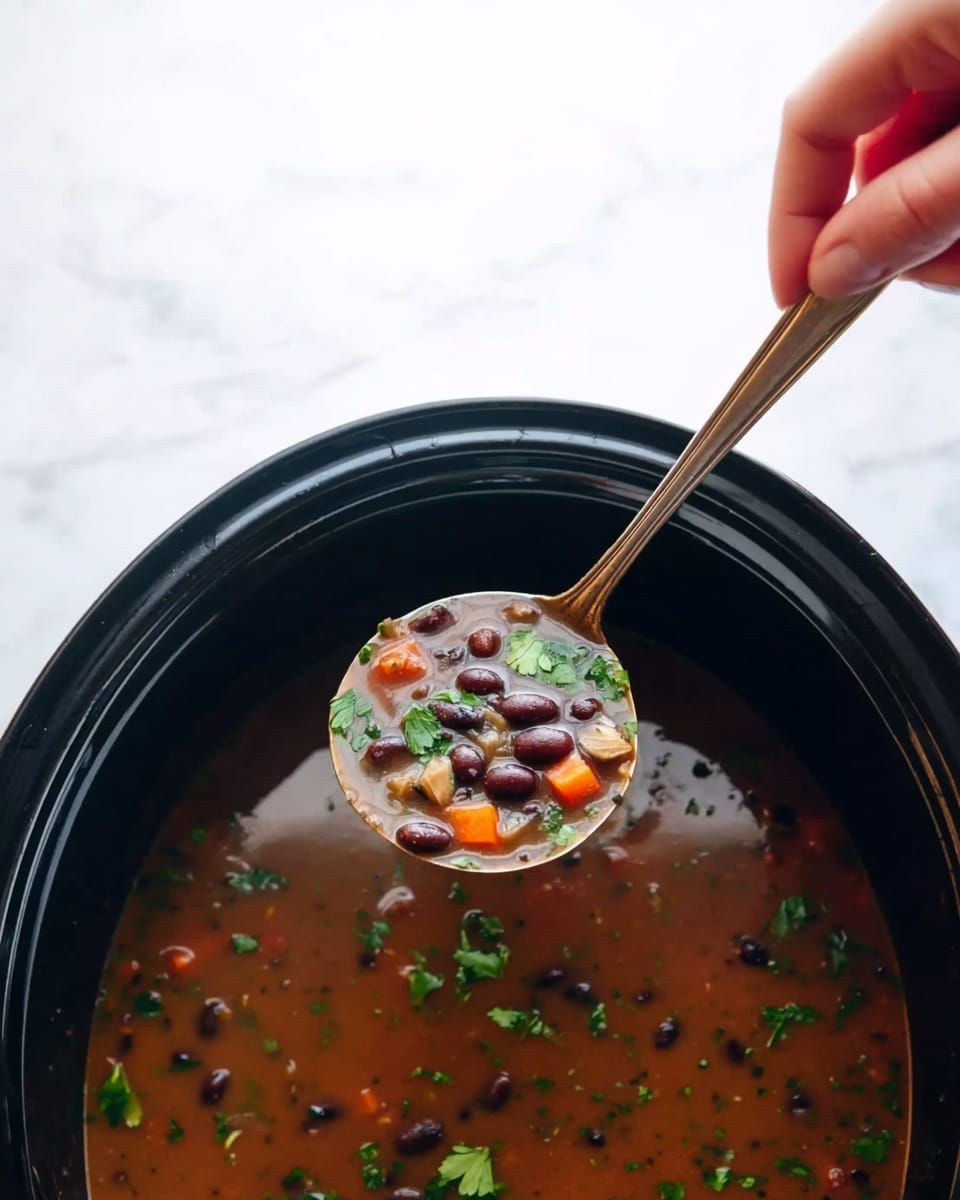 A black pot filled with brown soup containing black beans, small orange carrot pieces, and green herb leaves floating on top. A spoon is scooping up the soup, held by a woman's hand from above. The pot is placed on a white marbled surface. Photo taken with an iphone --ar 4:5 --v 7