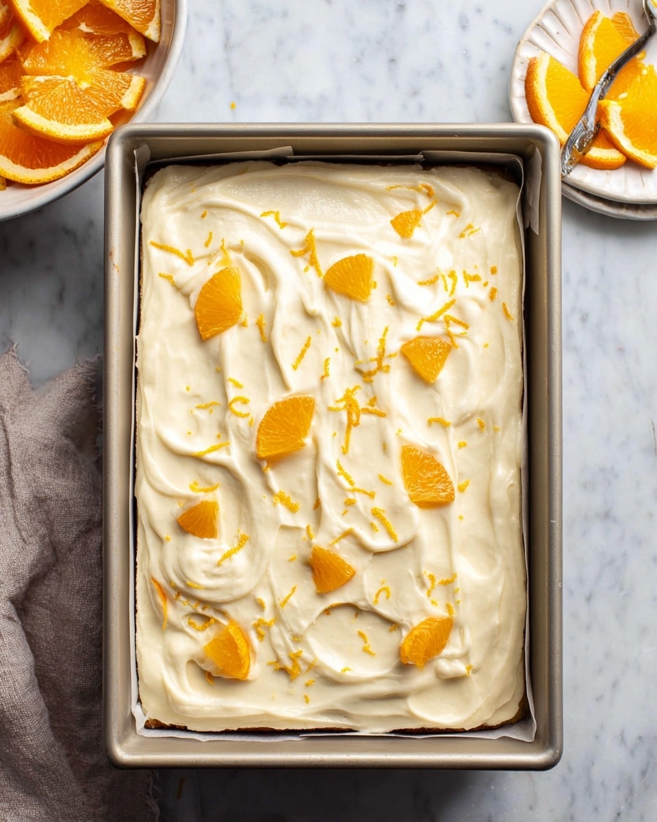 A rectangular cake in a baking pan lined with parchment paper sits on a white marbled surface. The cake has one visible layer covered with a thick, creamy white frosting spread with smooth swirls. Scattered on top are small bright orange slices and thin strips of orange zest, adding a pop of color and texture to the creamy surface. Nearby, a white bowl filled with orange slices and a white dish are partially visible, enhancing the fresh and citrus theme of the image. photo taken with an iphone --ar 4:5 --v 7