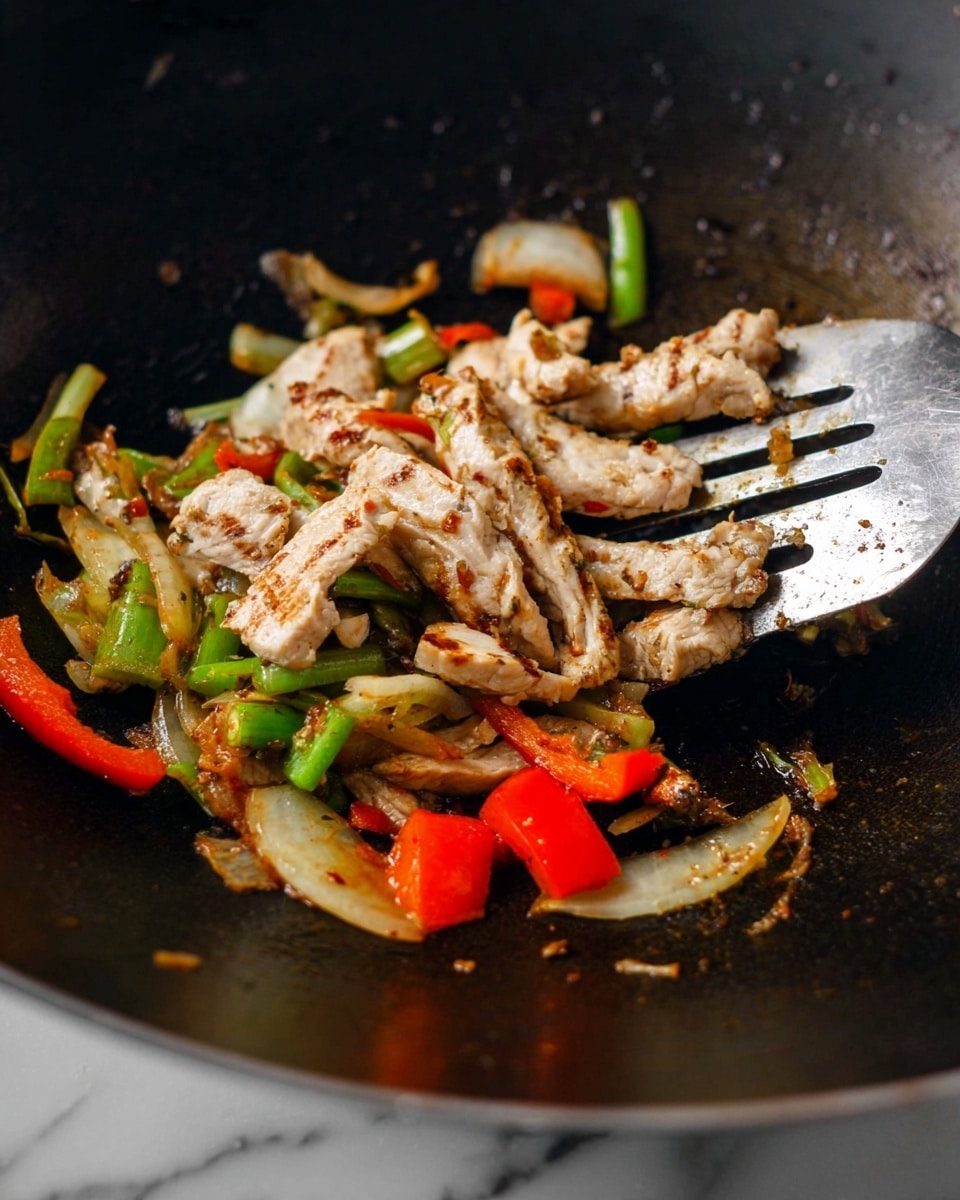 The image shows a black wok with cooked, thin pieces of white meat with light brown grill marks on top, sitting on a layer of sautéed vegetables including green celery, translucent onion slices, and small chunks of bright red bell pepper spread around. A metal spatula is partially lifting the meat and vegetables on the right side of the wok. The surface under the wok is a white marbled texture. photo taken with an iphone --ar 4:5 --v 7