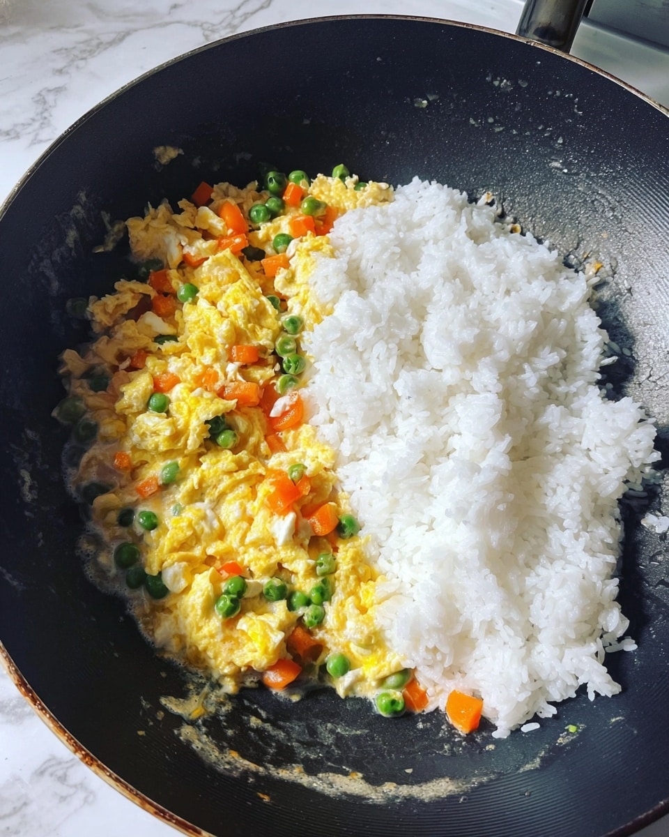 In a black wok, there is one layer of soft, shiny white rice placed on the right side. On the left side, there is a layer of yellow scrambled eggs mixed with small pieces of orange carrots, green peas, and green beans scattered within. The background shows a kitchen counter with a white marbled texture. photo taken with an iphone --ar 4:5 --v 7