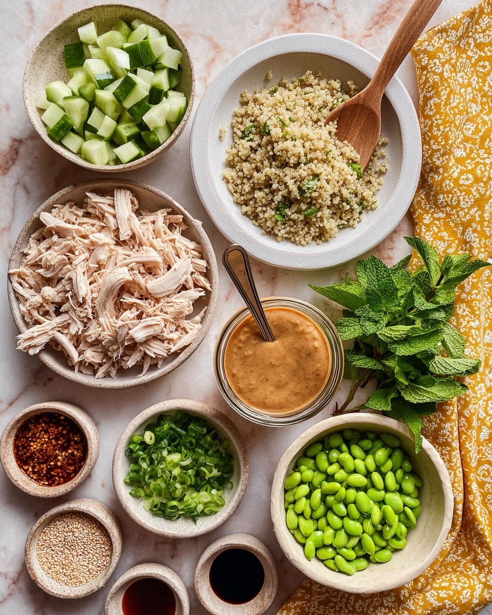 The image shows a flat white plate in the center with a pile of shredded light beige chicken meat. Above it, a white bowl filled with cooked quinoa with a wooden spoon resting inside. To the right, a bowl filled with green cubed cucumber pieces and a pile of fresh green herbs next to it on a white marbled surface. Below the cucumber, a glass jar filled with smooth light brown peanut sauce with a spoon inside. To the right, a small white bowl filled with bright green edamame beans. Below is a beige bowl with chopped green onions. To the left of the quinoa bowl is a small bowl with fresh dark green mint leaves, and on the left bottom, small cups filled with sesame seeds, soy sauce, and another sauce. The whole setup is on a white marbled surface with a yellow patterned cloth to the right. Photo taken with an iphone --ar 4:5 --v 7
