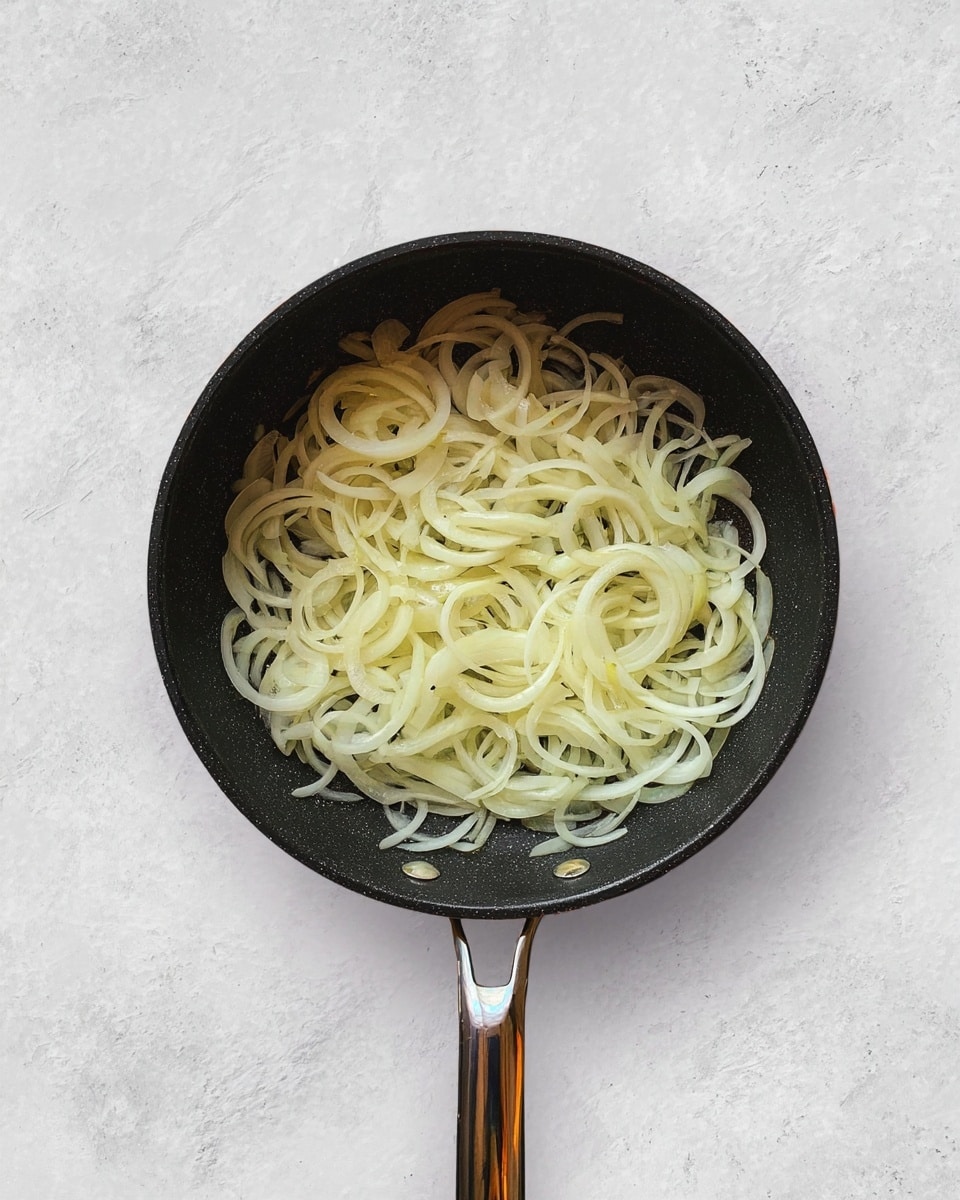 A black frying pan filled with thin, light yellow slices of onion spread evenly inside. The frying pan has a long metal handle and a small metal loop handle on the opposite side. The background is a white marbled texture. Photo taken with an iphone --ar 4:5 --v 7