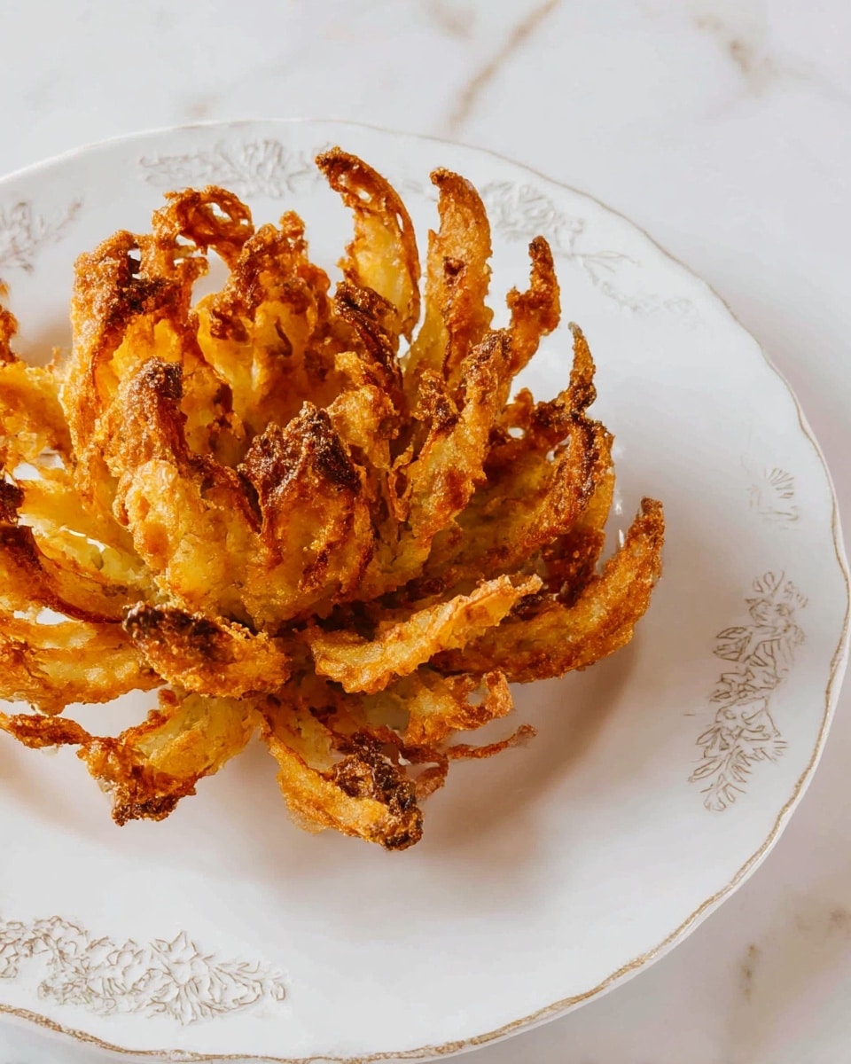A single fried blooming onion sits in the center of a white plate with delicate embossed patterns around the rim. The onion is golden brown with crispy, uneven petals that curl upwards and outwards, showing a crunchy texture with darker edges where it is more fried. The petals are layered densely, creating a flower-like shape with a rough, crunchy surface. The plate rests on a white marbled surface. photo taken with an iphone --ar 4:5 --v 7