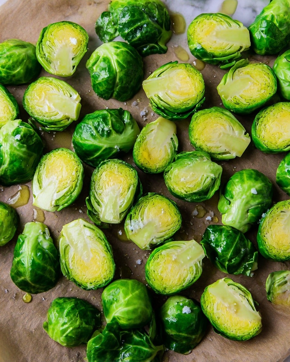 The image shows many bright green Brussels sprouts halved and spread out on a brown baking paper set on a white marbled surface. The sprouts have a fresh, shiny look with some outer dark green leaves loose around them. The cut sides of the sprouts reveal layers of light yellow and green inside. Small chunks of coarse white salt and drops of golden oil are sprinkled over the Brussels sprouts, adding texture and shine. The overall look is fresh and ready for cooking. photo taken with an iphone --ar 4:5 --v 7