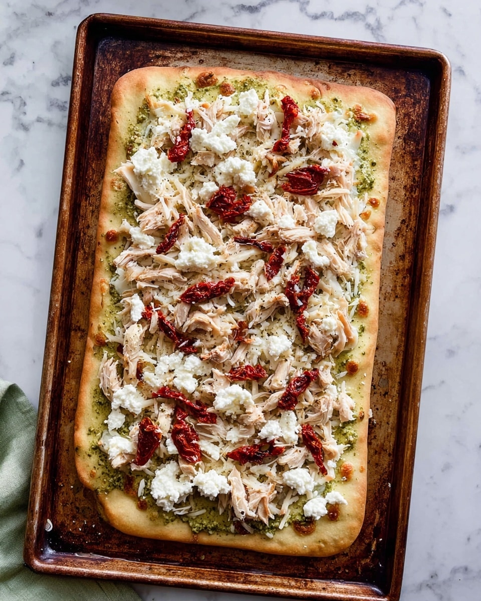 A rectangular flatbread pizza on a large, worn, brown baking tray sits on a white marbled surface. The flatbread is golden brown with slightly puffed and crispy edges. The first layer is a greenish pesto spread evenly across the base, visible near the edges. On top of the pesto is a generous layer of shredded white mozzarella cheese that covers the entire flatbread. Scattered over the cheese are pieces of light beige shredded cooked chicken. Dollops of soft, white ricotta cheese are spaced out above the chicken, adding a creamy texture. Sun-dried tomatoes, deep red in color and slightly wrinkled, are evenly spread on the top. photo taken with an iphone --ar 4:5 --v 7
