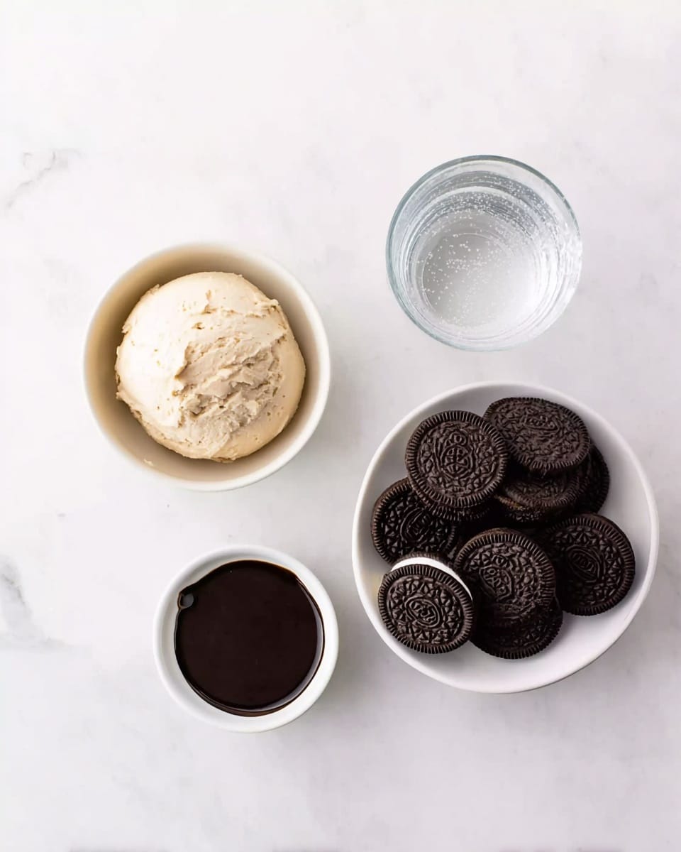The image shows three white bowls on a white marbled surface. The first bowl contains a round mound of light beige cream or dough with a smooth texture. The second bowl has nine dark chocolate sandwich cookies with embossed patterns on top, arranged loosely. The third small bowl holds a thick, dark brown liquid, possibly chocolate sauce. To the right of these bowls is a clear glass of water with visible condensation. photo taken with an iphone --ar 4:5 --v 7