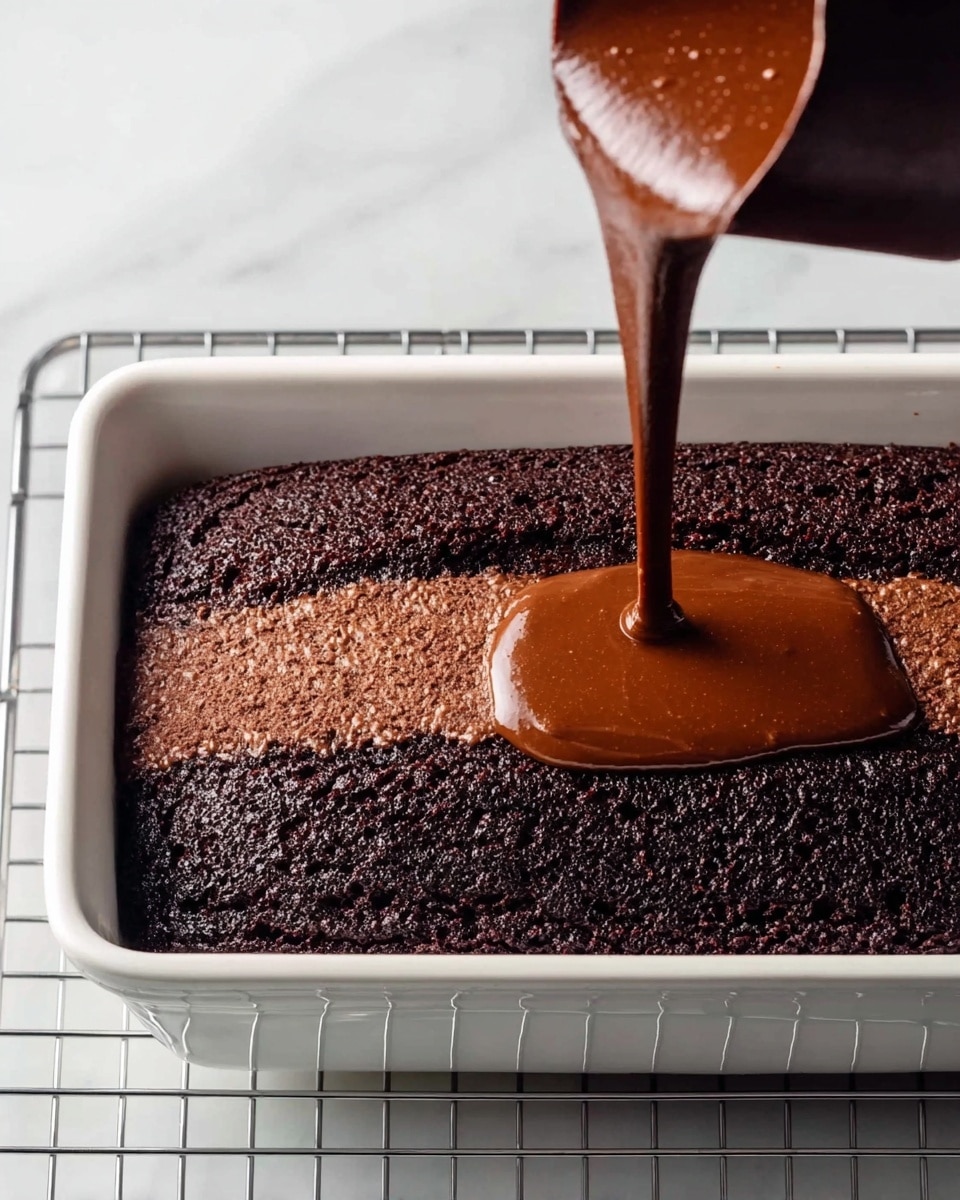 A dark brown chocolate cake sits in a white rectangular loaf pan on a wire cooling rack over a white marbled surface. A lighter brown chocolate batter is being poured in a thick stream from a dark brown measuring cup onto the center of the darker cake layer in the pan. The textures of the two chocolate layers contrast with the rough, baked surface of the cake and the smooth, flowing batter. Photo taken with an iphone --ar 4:5 --v 7
