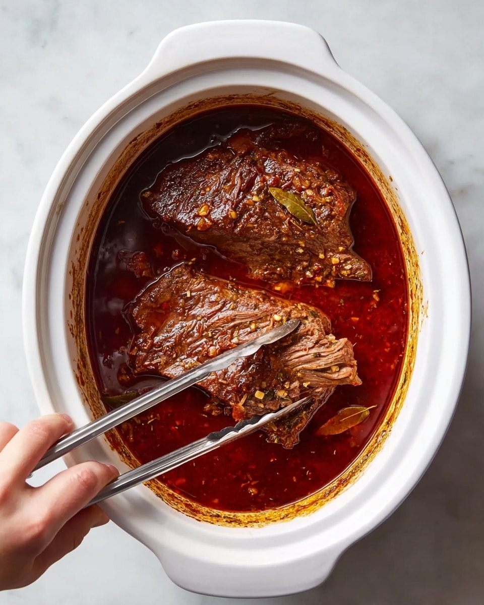 A white oval slow cooker filled with two large pieces of cooked meat soaking in a rich dark red sauce with visible herbs and spices. The meat looks tender with a rough texture and is being lifted by metal tongs held by a woman's hand from the lower left corner. The cooker sits on a white marbled background, with slight brown stains marking the inner rim where the sauce has splashed. Photo taken with an iphone --ar 4:5 --v 7