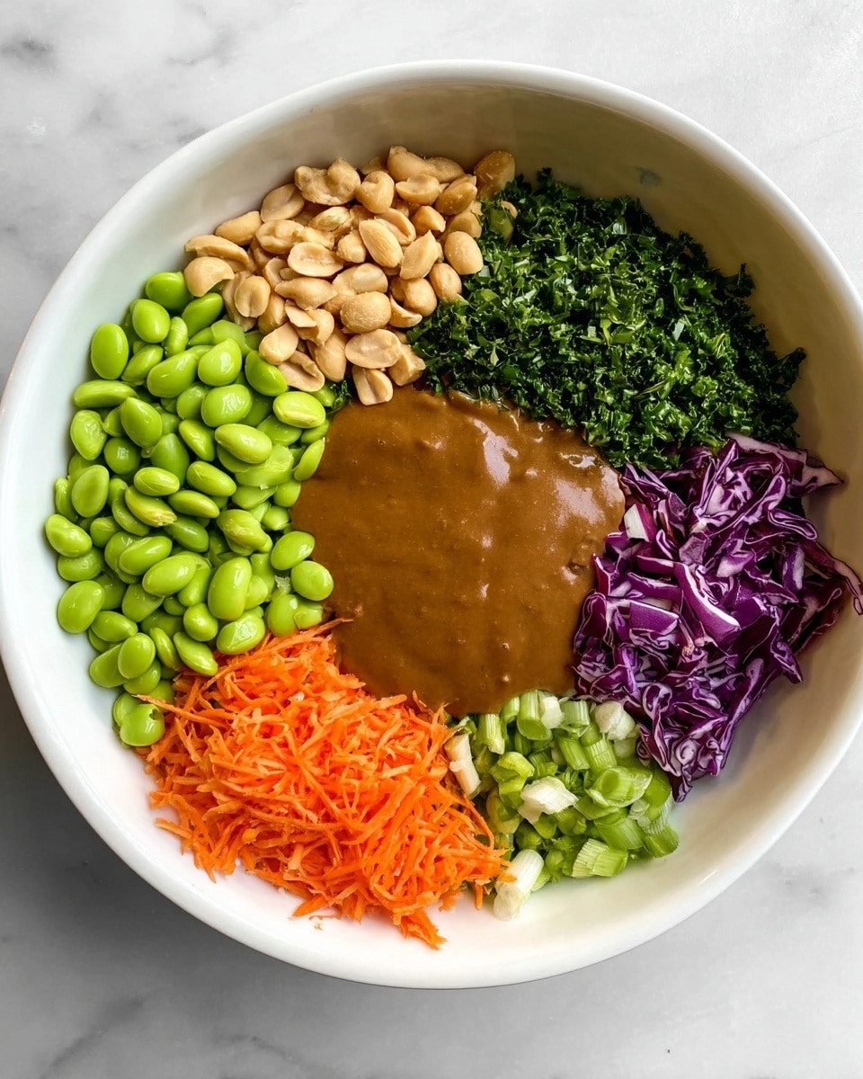 A white bowl filled with six main layers arranged side by side. Starting from the left, there is a large pile of bright green edamame beans with a smooth, shiny texture. Next to it is a cluster of light tan peanuts with a slightly rough surface. Above the peanuts is a layer of dark green chopped kale, followed by a dense pile of finely chopped green herbs, adding a fresh look. To the right of the herbs is a small portion of sliced light green scallions, then a section of finely shredded purple cabbage. Covering the center and slightly overlapping some vegetables is a smooth, thick layer of brown sauce with a creamy texture. A small pile of bright orange shredded carrots is placed along the bottom right edge of the sauce. The bowl sits on a white marbled surface. Photo taken with an iphone --ar 4:5 --v 7