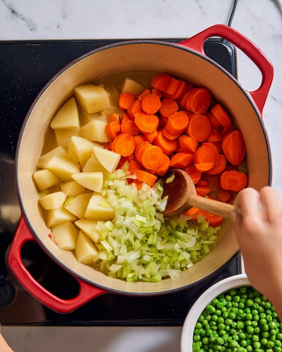 A large red pot placed on a black stove contains three layers of ingredients being stirred. The bottom layer is light yellow and translucent chopped onions. The middle layer consists of medium green chopped celery. The top layer includes bright orange sliced carrots along with pale yellow cubed potatoes. On the right side of the pot, there is a white bowl filled with green peas. A woman's left hand holds one handle of the pot, and a woman's right hand stirs the vegetables with a wooden spoon inside the pot. The background and surface are white marbled texture. photo taken with an iphone --ar 4:5 --v 7