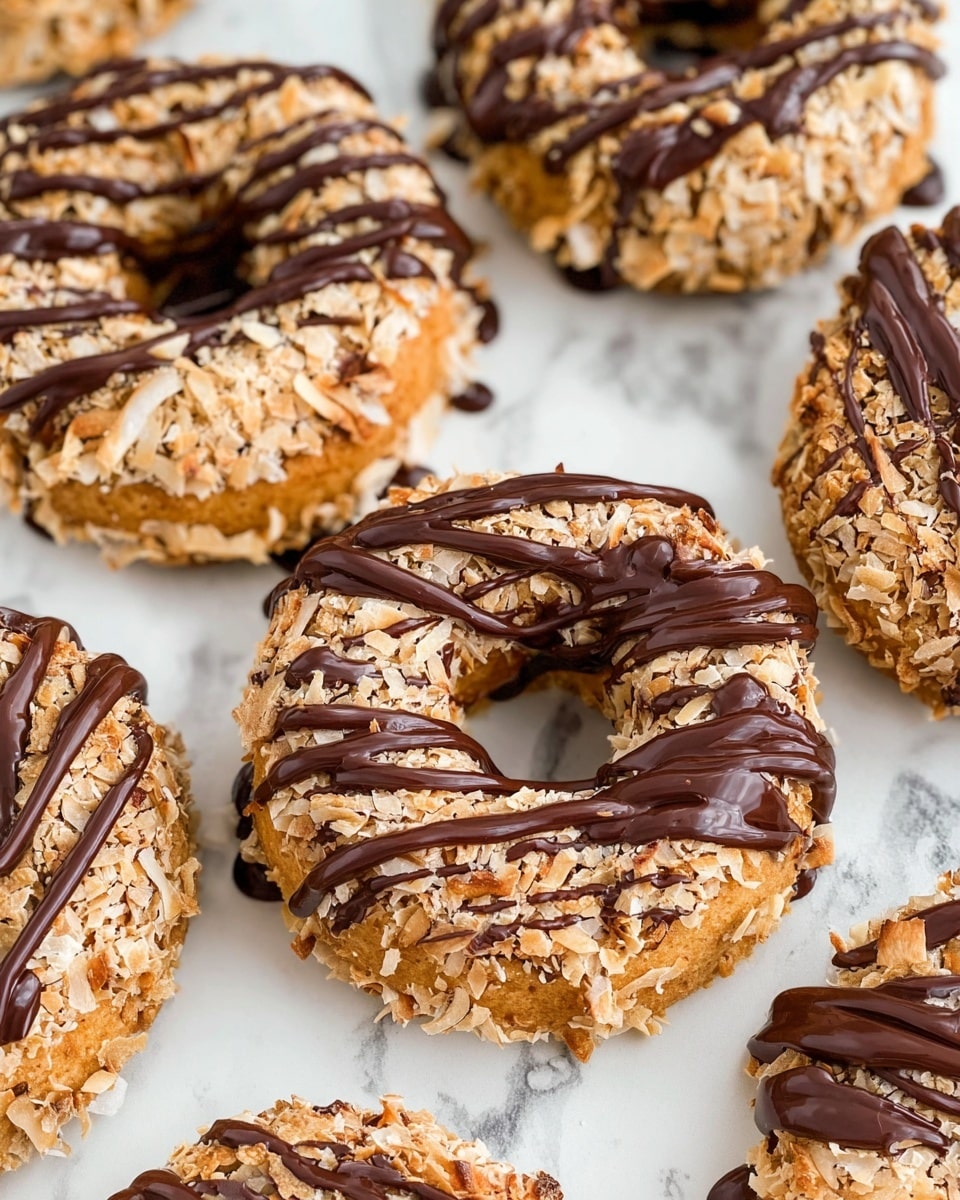 Several round donuts lay on a white marbled surface, each with three main layers visible: the base donut layer is light golden brown, the top layer is fully covered with toasted light brown coconut flakes giving a rough texture, and a glossy dark chocolate drizzle decorates the top with thin lines and a thicker stripe across part of the donut, adding contrast and shine. Photo taken with an iphone --ar 4:5 --v 7